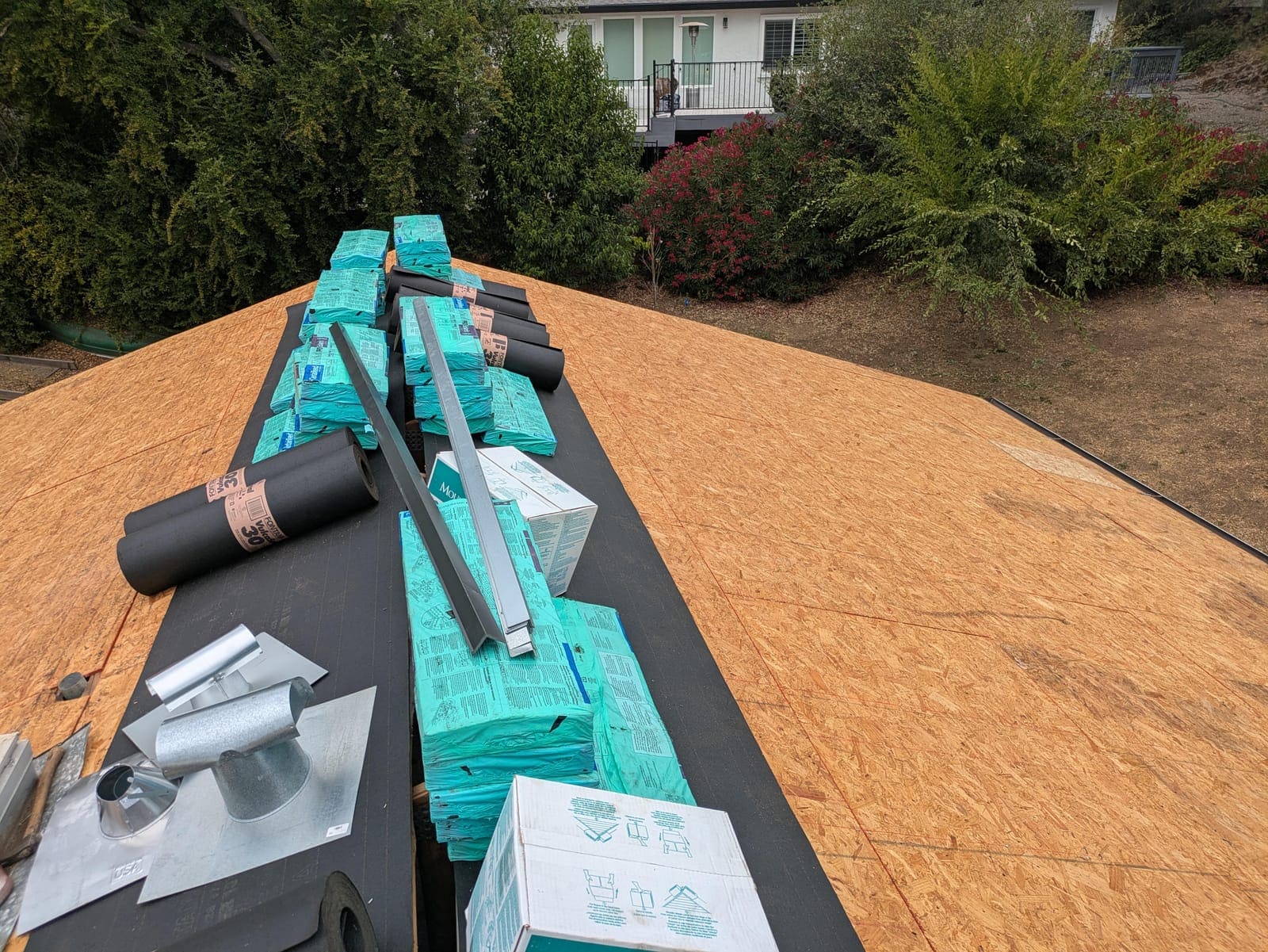 Underlayment partially installed with shingle bundles, vents, and flashings staged on the roof